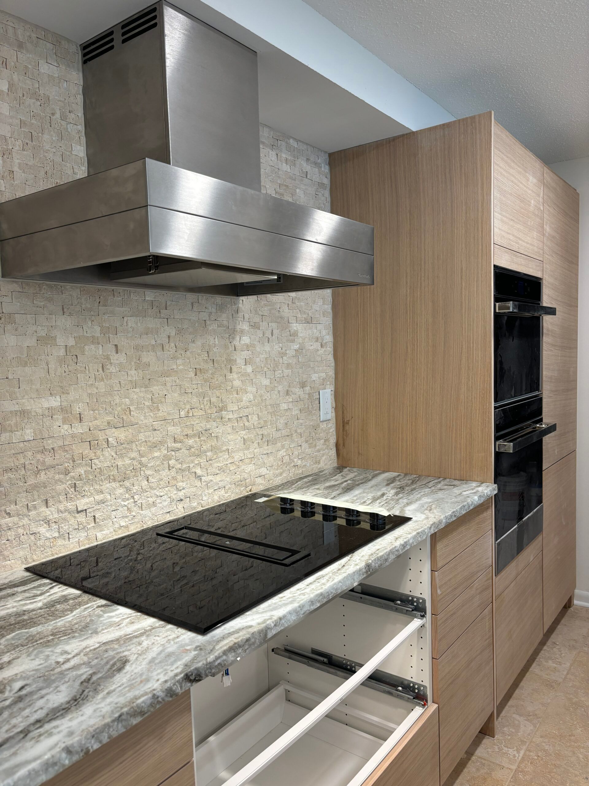 Modern kitchen with stainless range hood, cooktop, marble island, and built-in oven cabinet