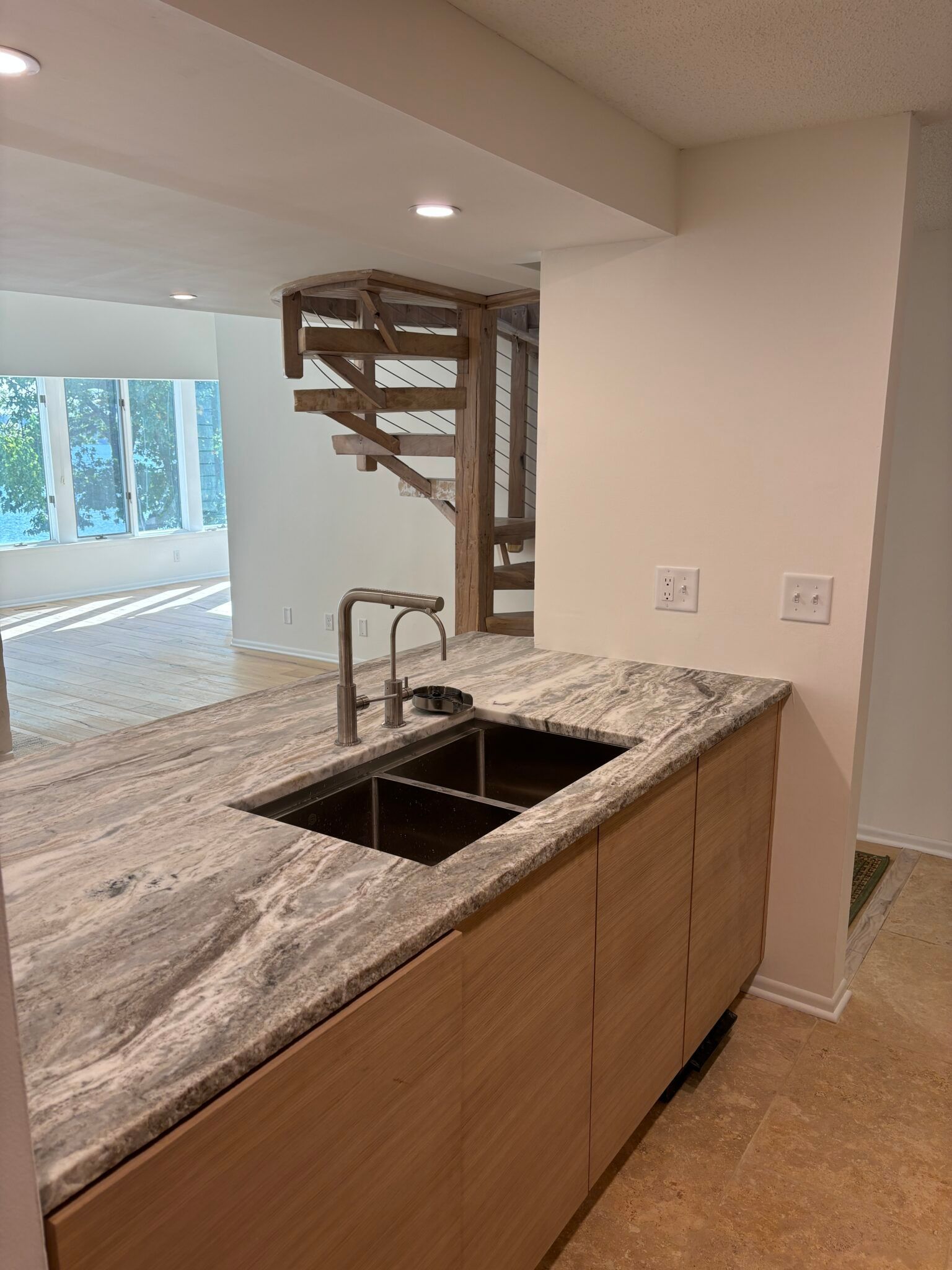 Modern kitchen island with granite countertop, double sink, and wooden staircase in the background