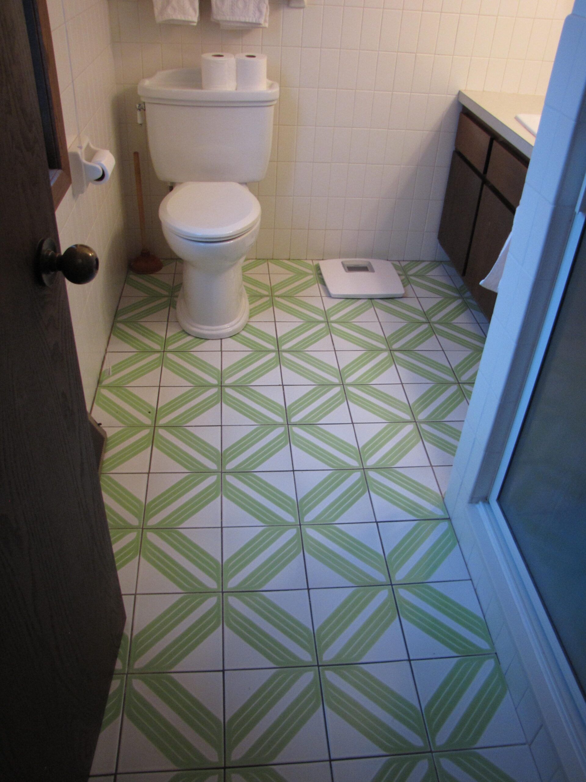 Small bathroom with white toilet and green geometric tile floor, viewed through an open doorway