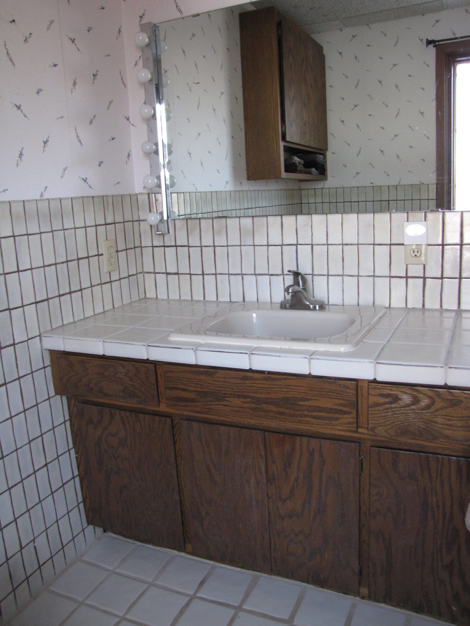 Small bathroom vanity with sink, mirror, tiled walls, and wood cabinets.