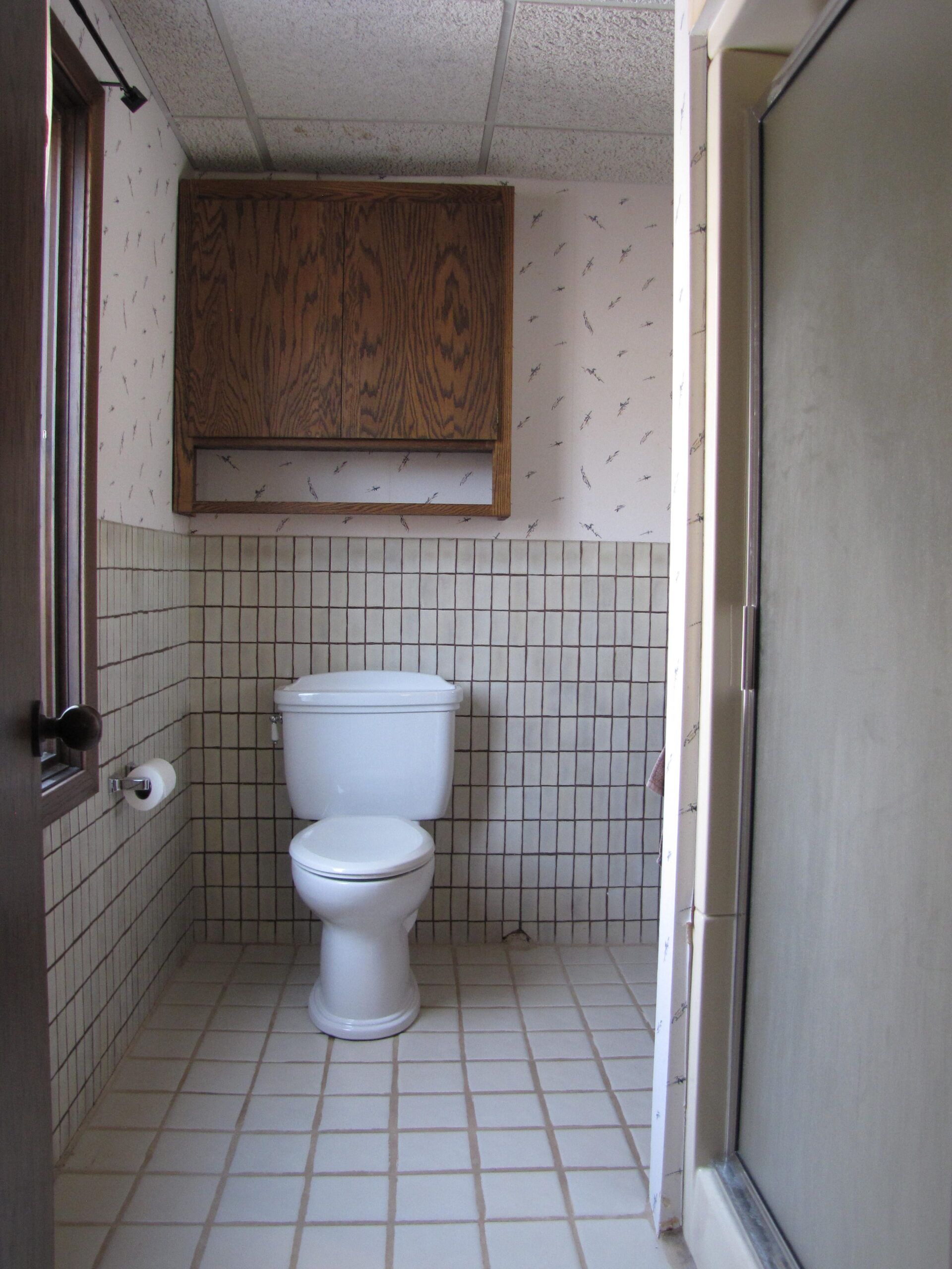 Small bathroom with a toilet, tiled walls and floor, and a cabinet above the toilet.