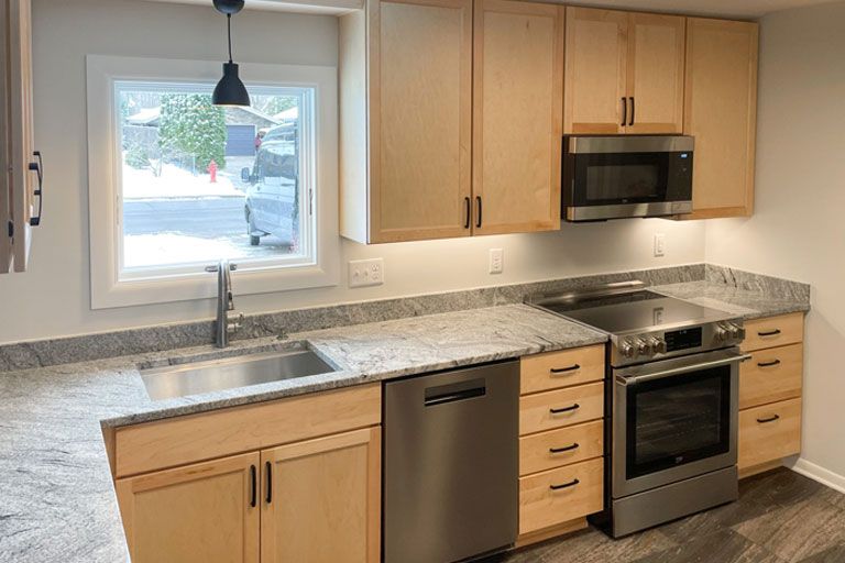 Modern kitchen with light wood cabinets, granite counters, stainless appliances, and a window over the sink