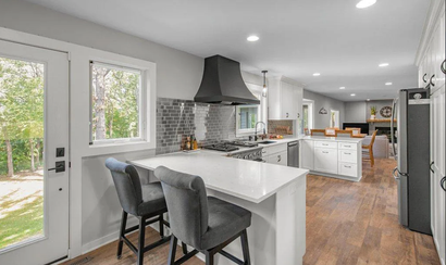 Bright modern kitchen with white island, gray stools, black range hood, and hardwood floors Bright modern kitchen with white island, gray stools, black range hood, and hardwood floors