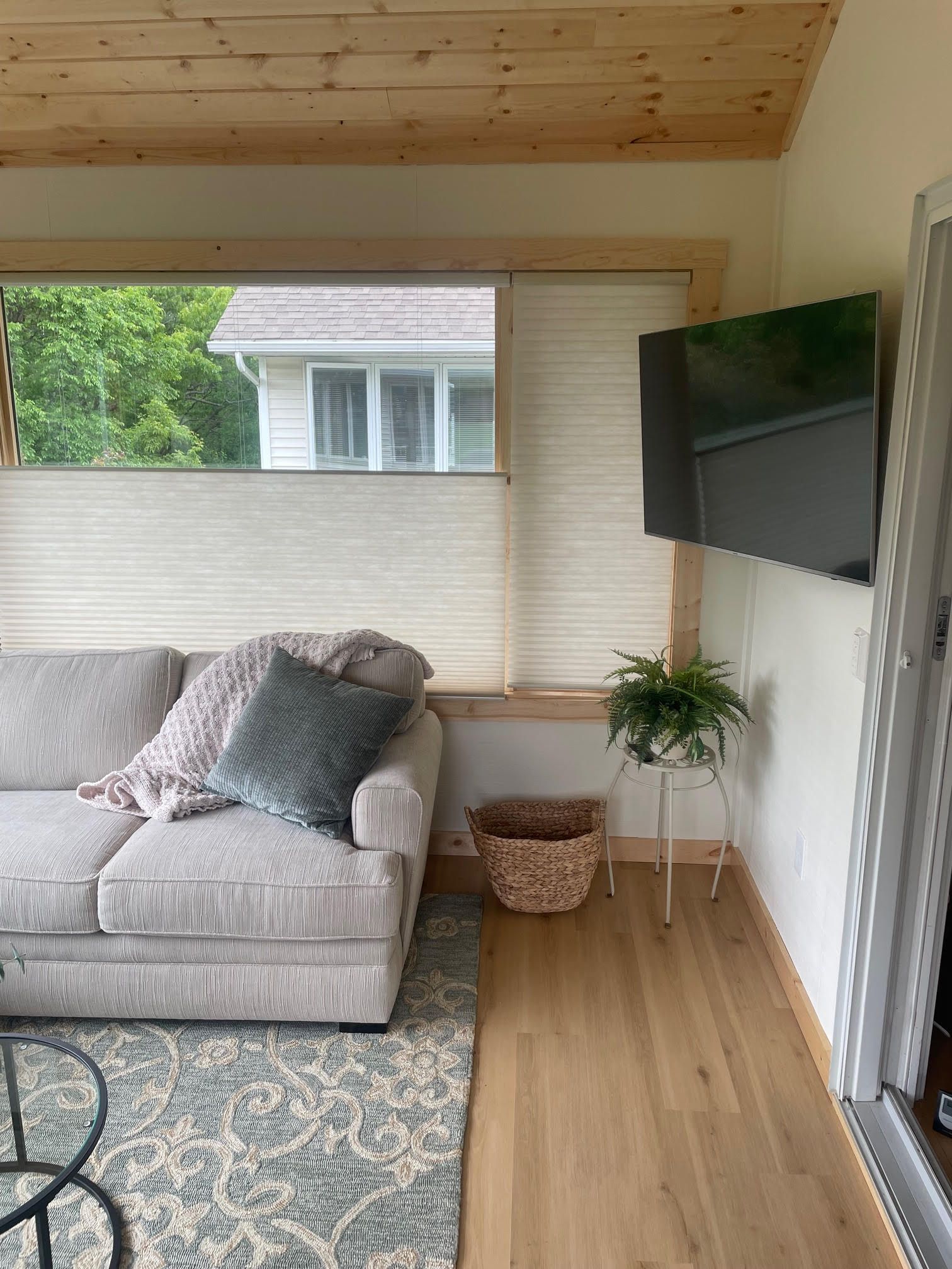 Cozy sunroom with a gray couch, wall-mounted TV, plant, woven basket, and wood-paneled walls