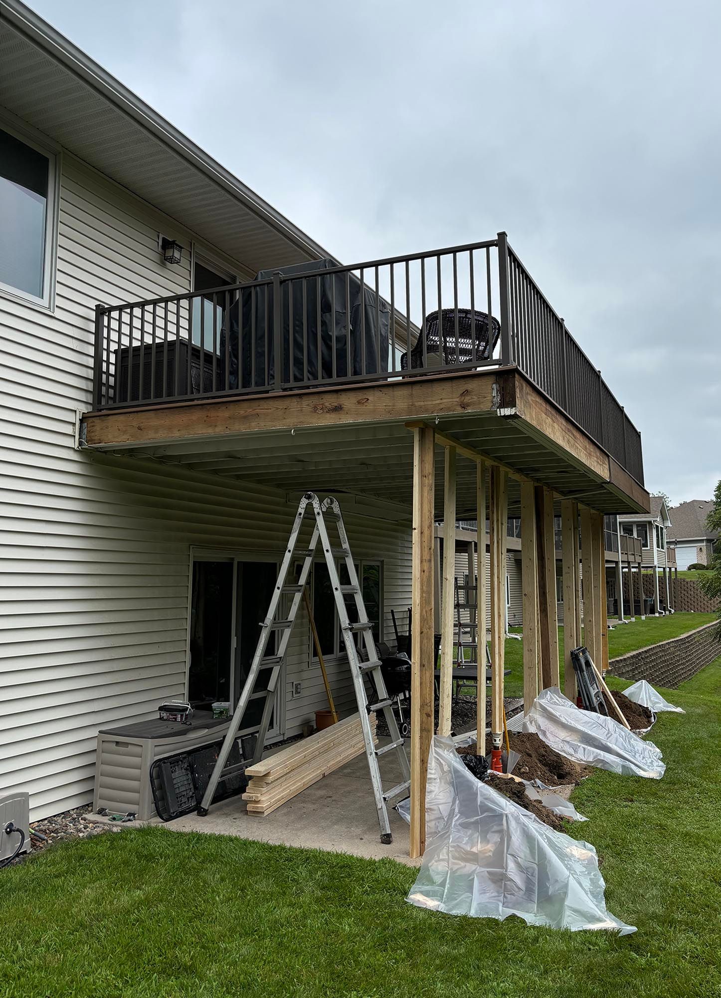 Raised wooden deck under construction on the back of a house, with ladders and support posts.