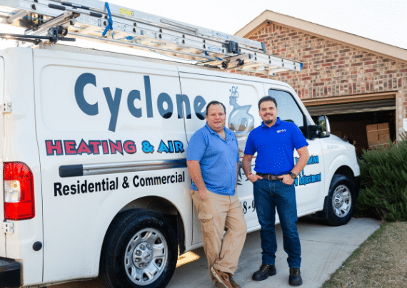 two men are standing in front of a cyclone heating and air van