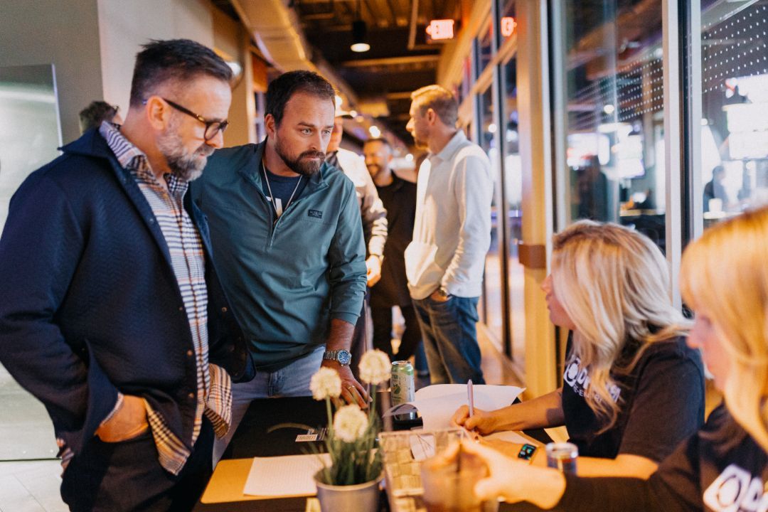 A group of people are standing around a table talking to each other.