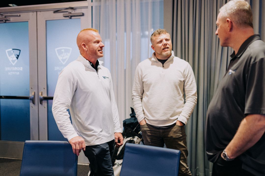 Three men are standing in a room talking to each other.