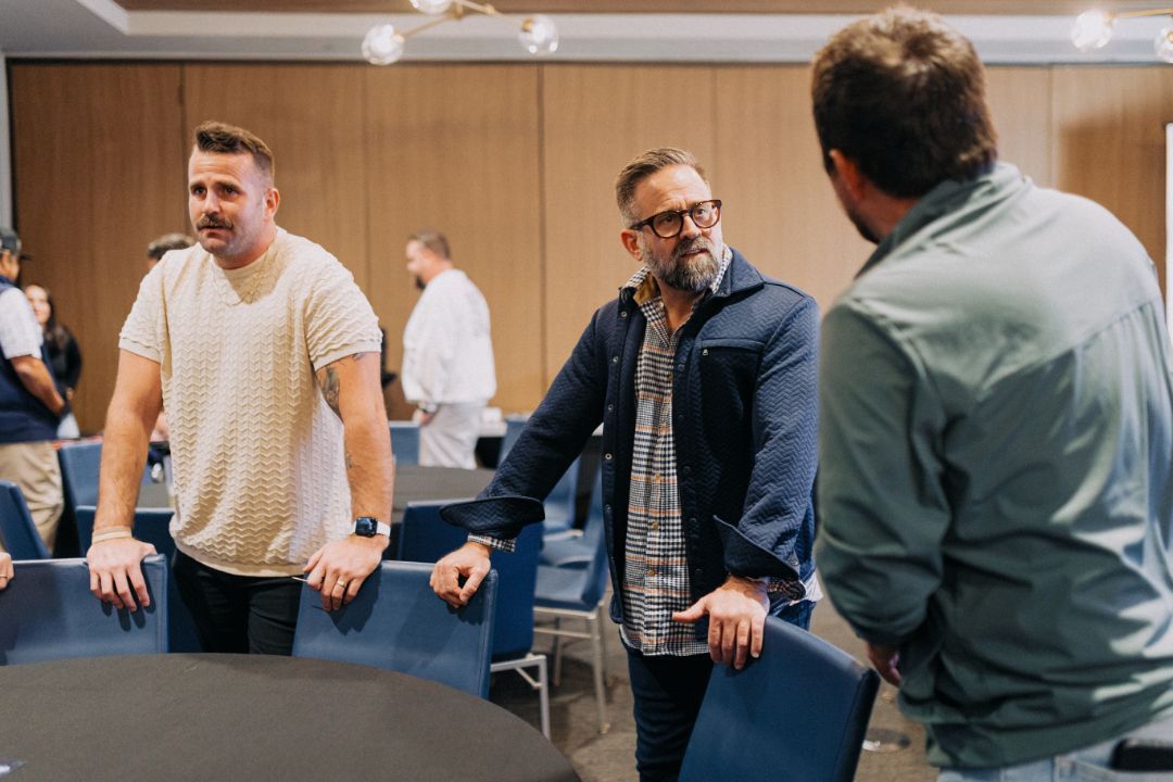 A group of men are standing around a table talking to each other.