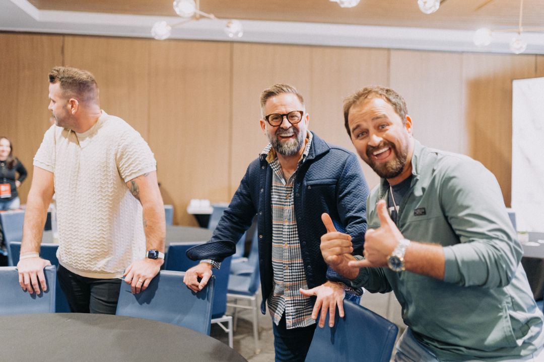 Three men are posing for a picture in a room and one of them is giving a thumbs up.