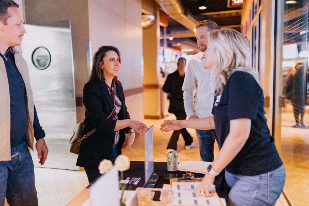 A group of people are standing around a table talking to each other.