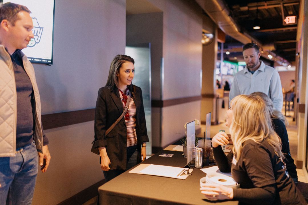 A group of people are standing around a table talking to each other.