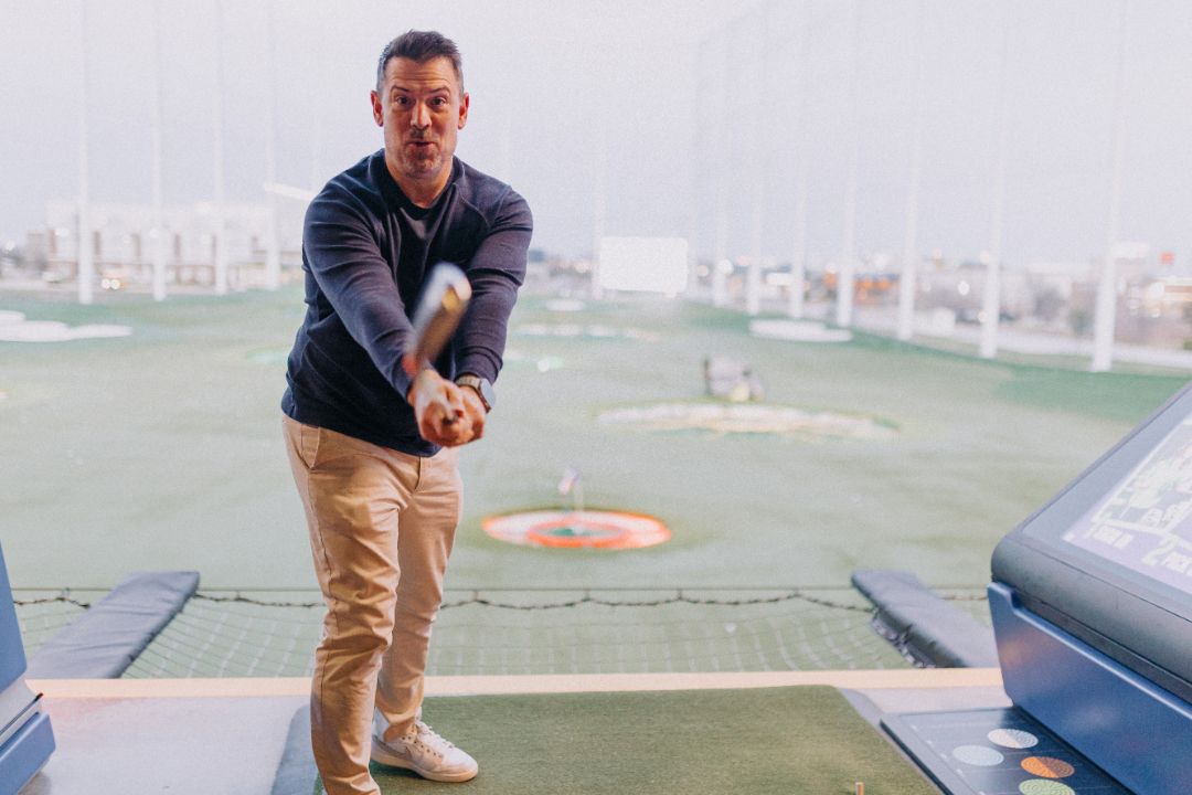 A man is swinging a baseball bat on a golf course.