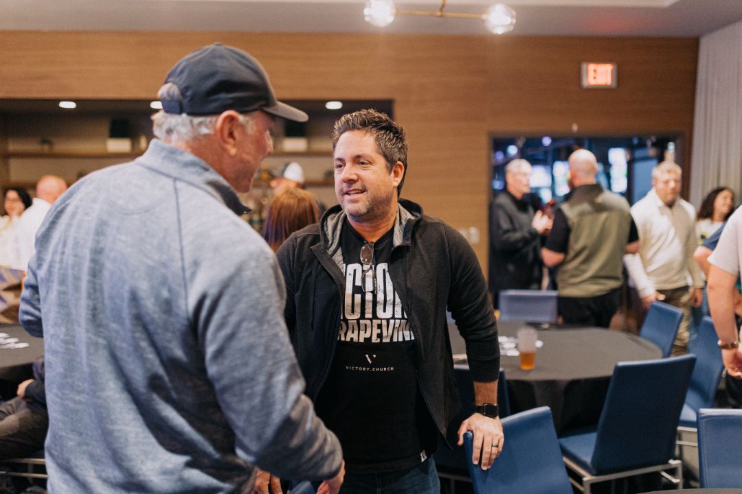 Two men are talking to each other in a room with tables and chairs.
