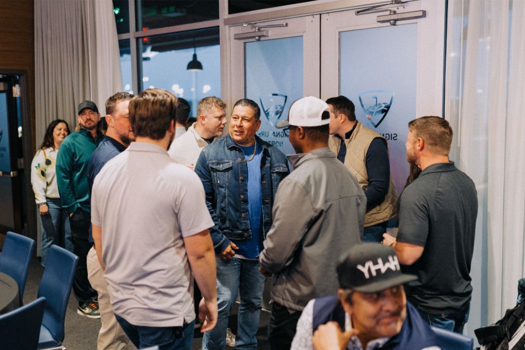 A group of men are standing in a room talking to each other.