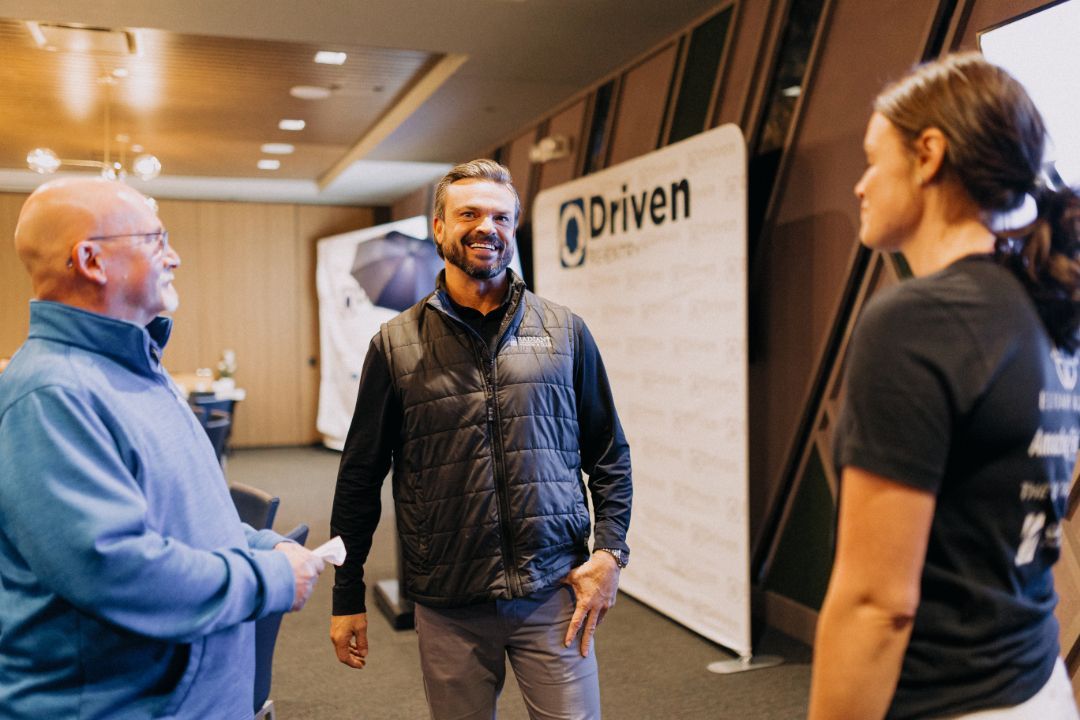 A group of people are standing in front of a sign that says driven.