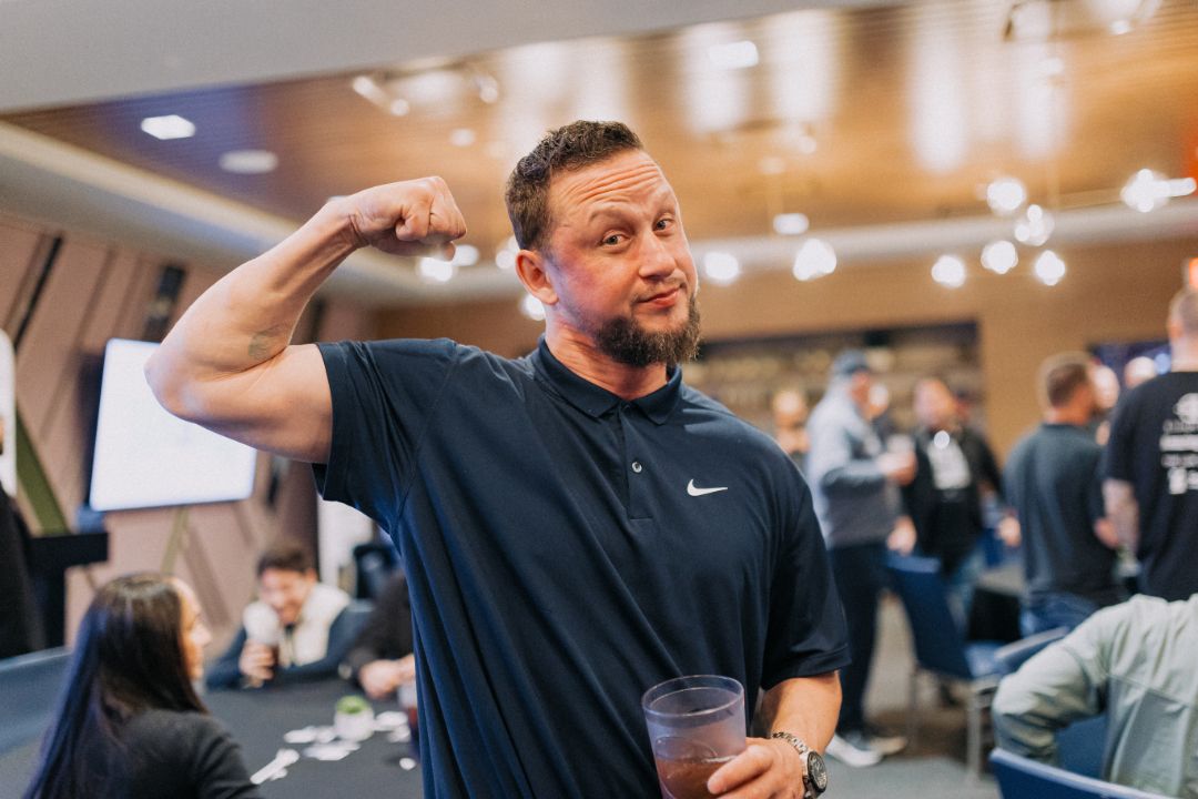 A man is flexing his muscles while holding a drink in a room.