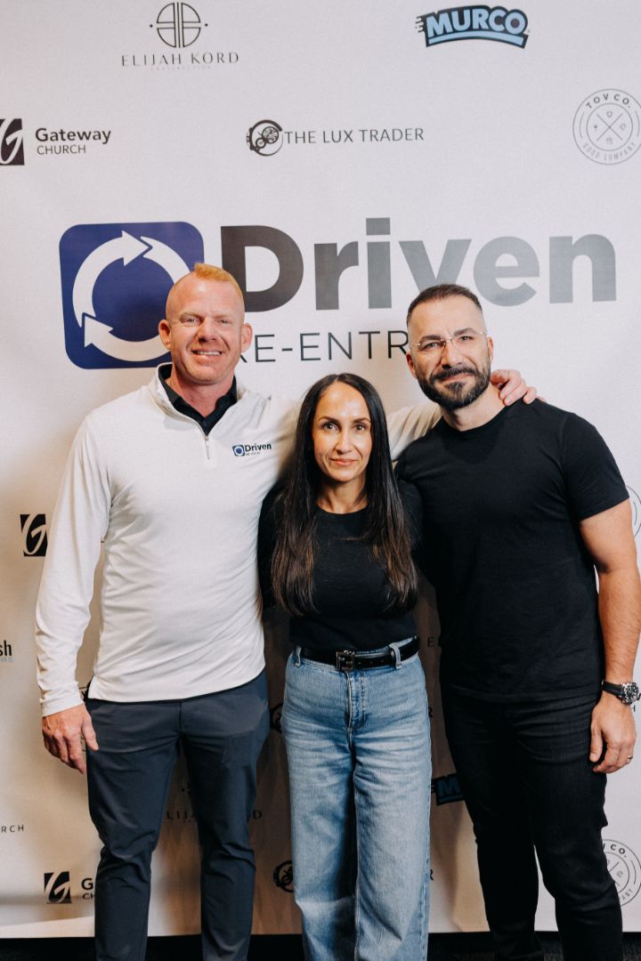 Three people are posing for a picture in front of a sign that says driven.