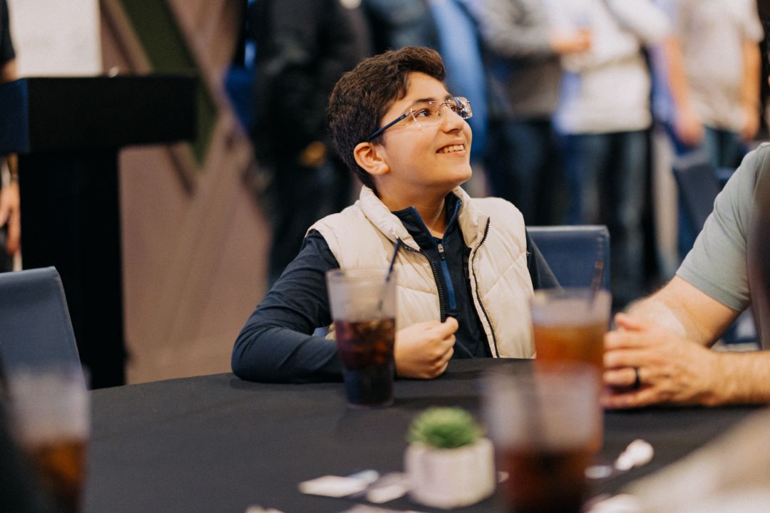 A young boy is sitting at a table with a glass of soda.