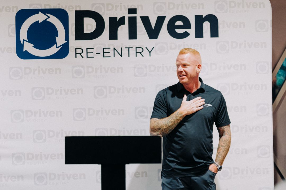 A man is standing in front of a sign that says driven