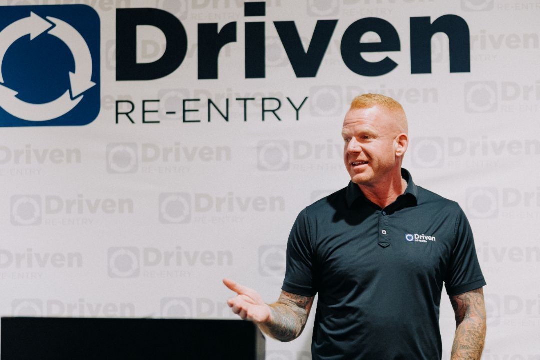 A man is standing in front of a sign that says driven