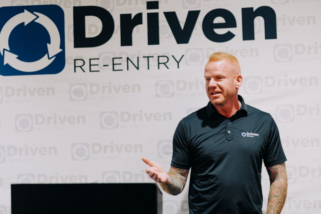 A man is standing in front of a sign that says driven