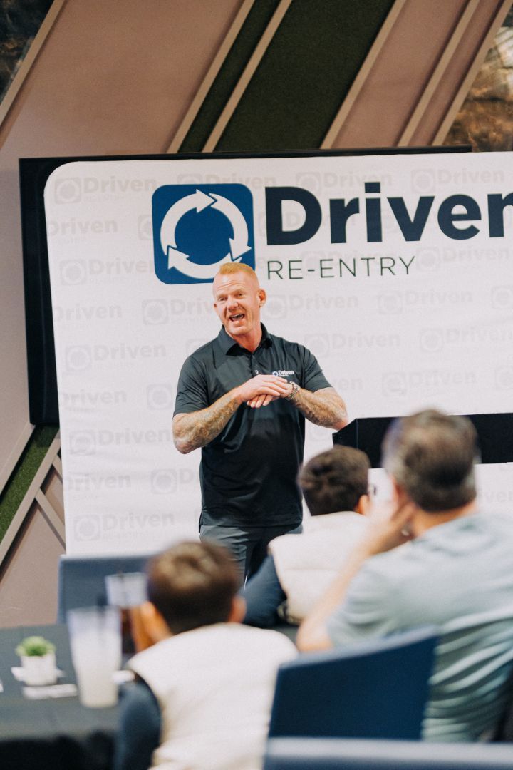A man is giving a presentation in front of a sign that says driver re-entry