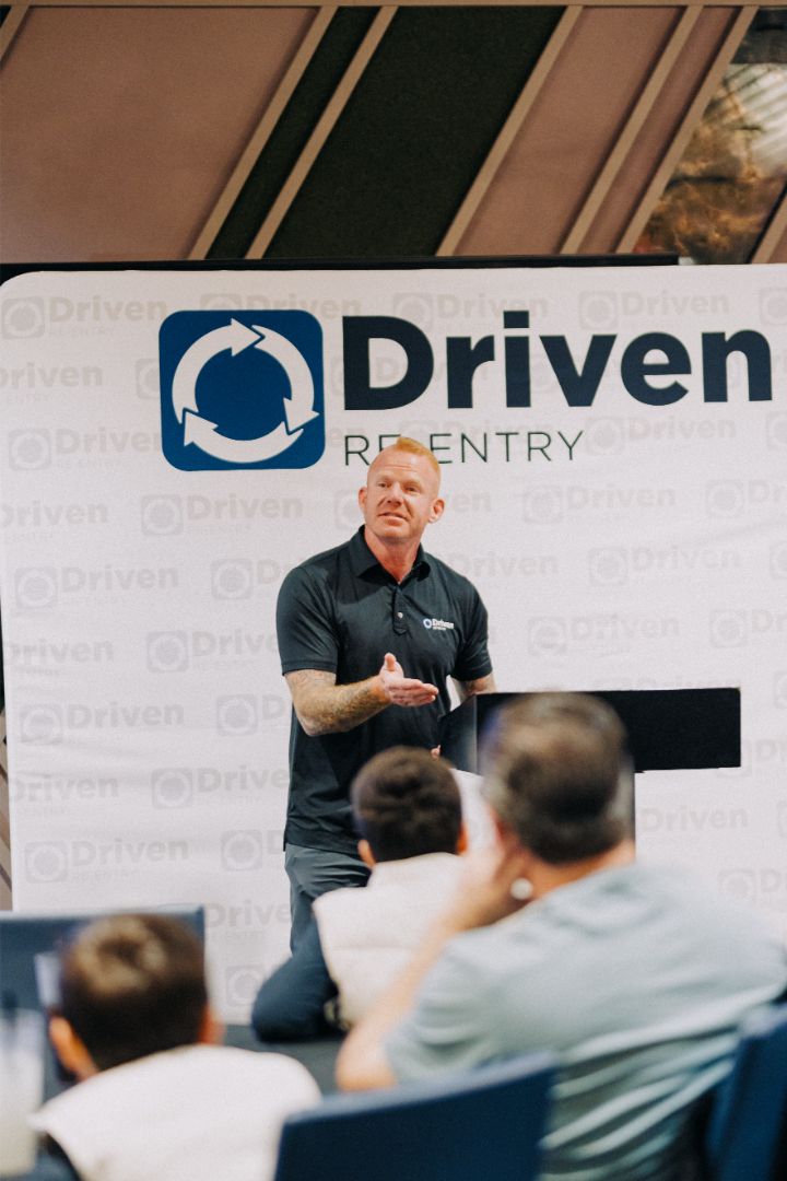 A man is giving a presentation in front of a sign that says driven