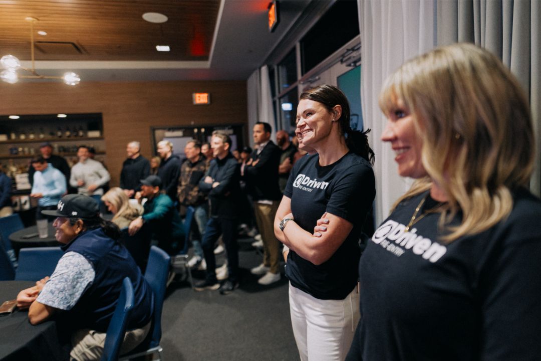 Two women are standing in front of a crowd of people in a room.