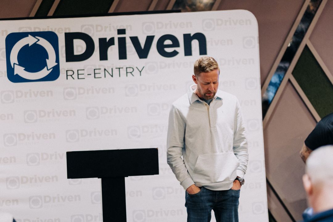 A man stands in front of a sign that says driven re-entry