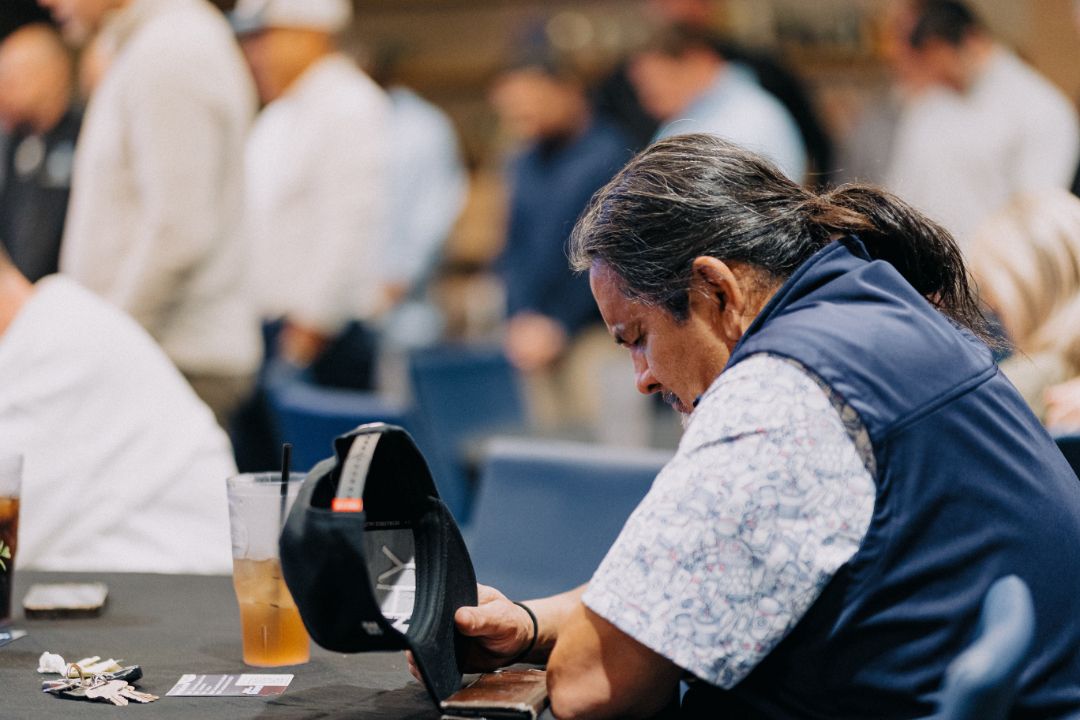 A man is sitting at a table looking at a hat.