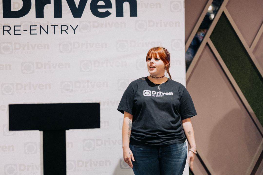 A woman is standing in front of a sign that says driven re-entry