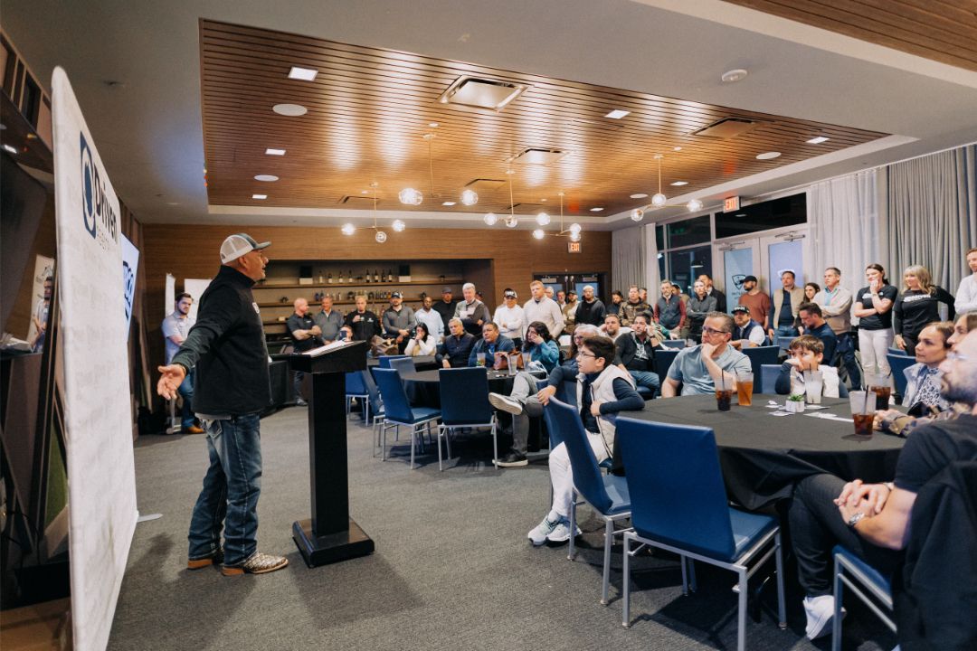 A man is standing at a podium in front of a large group of people sitting at tables.
