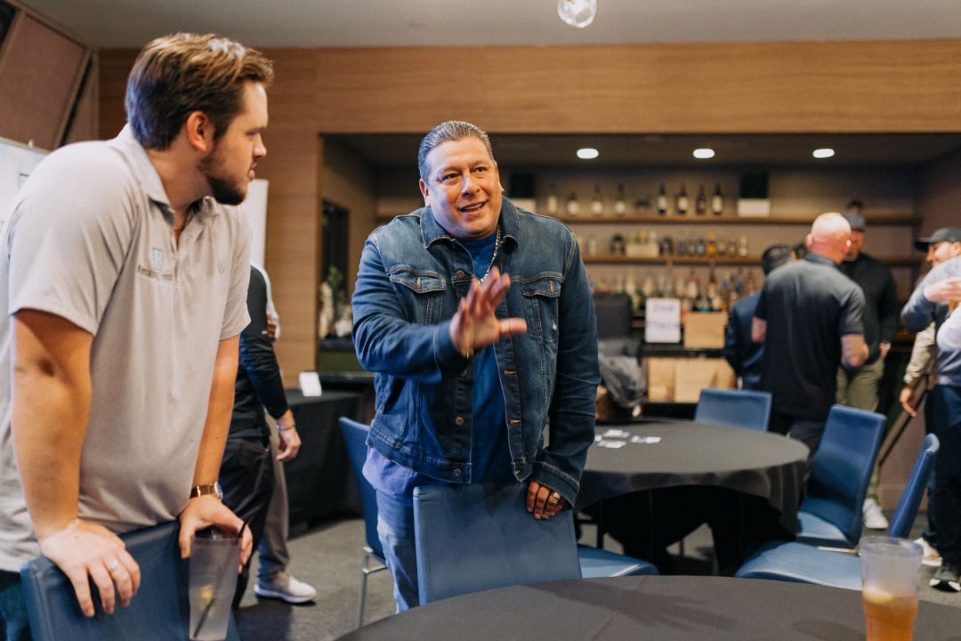 Two men are standing next to each other in a room talking to each other.