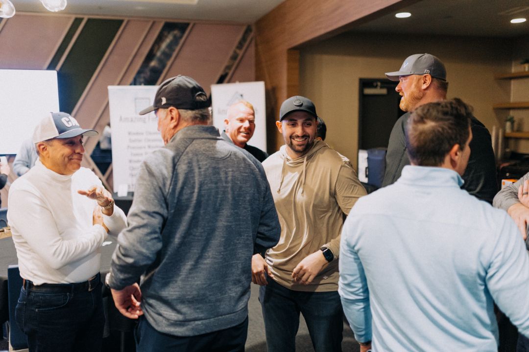 A group of men are standing in a room talking to each other.