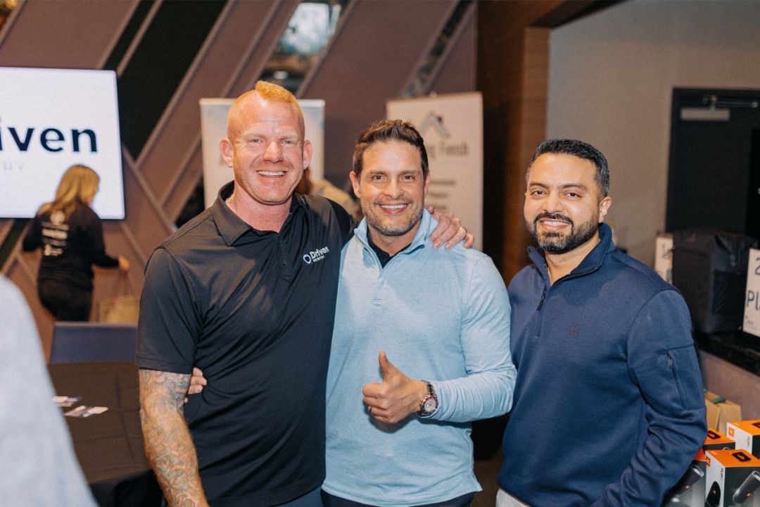 Three men are posing for a picture and one of them is giving a thumbs up.