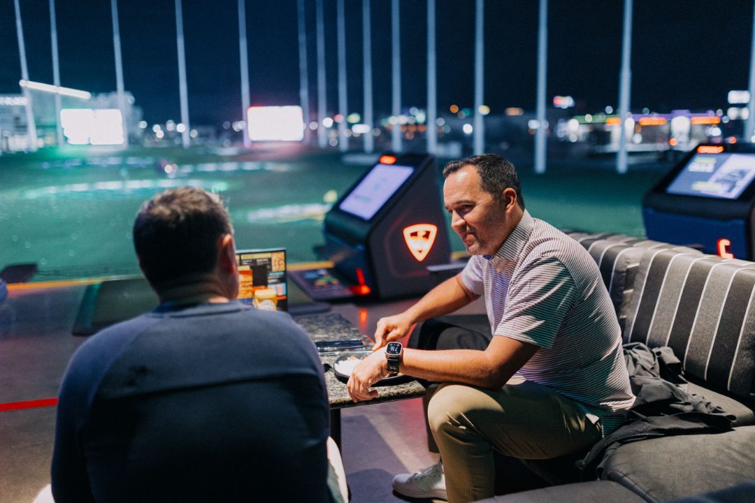 Two men are sitting on a couch talking to each other.