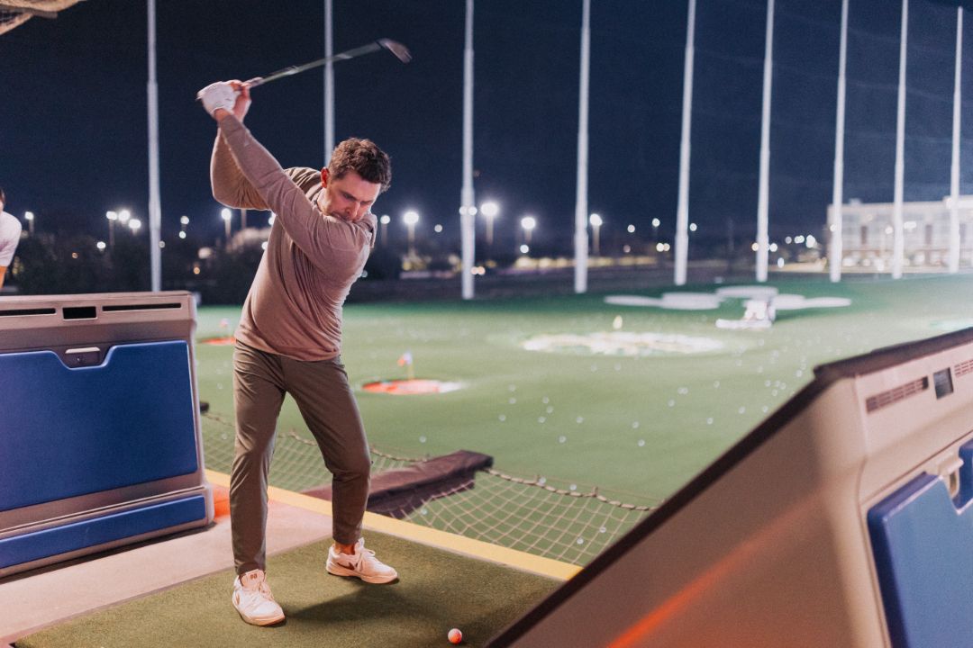 A man is swinging a golf club on a golf course at night.