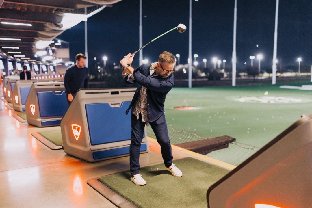 A man is swinging a golf club on a golf course at night.