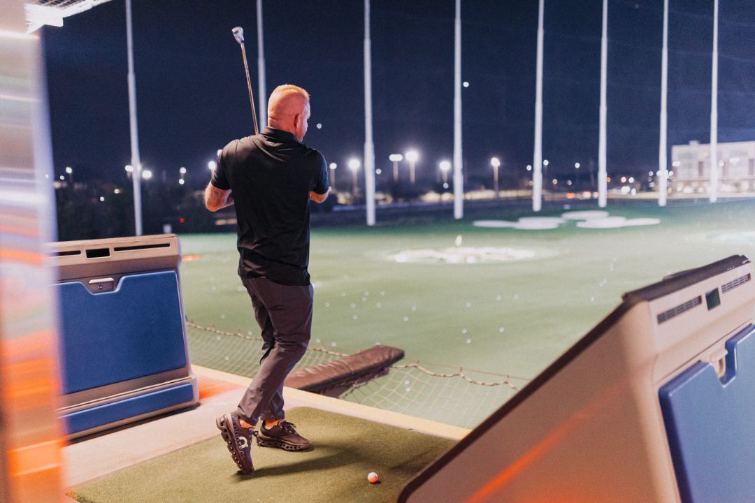 A man is swinging a golf club on a golf course at night.