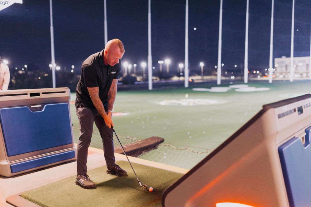 A man is swinging a golf club on a golf course at night.