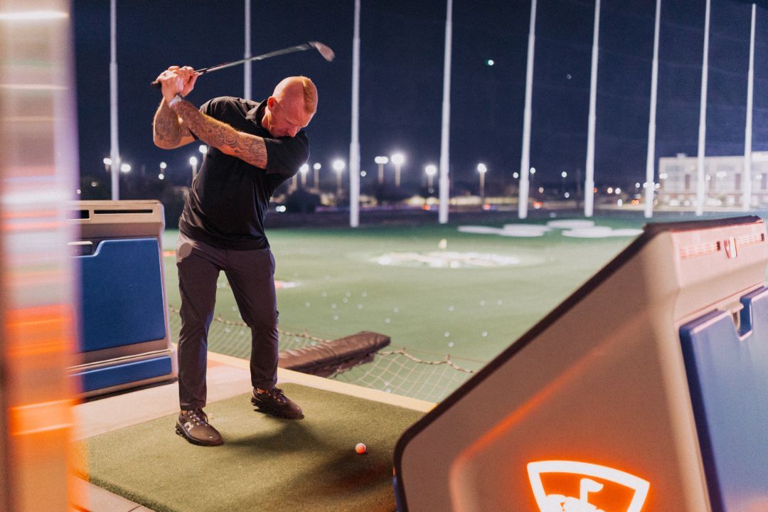 A man is swinging a golf club on a golf course at night.