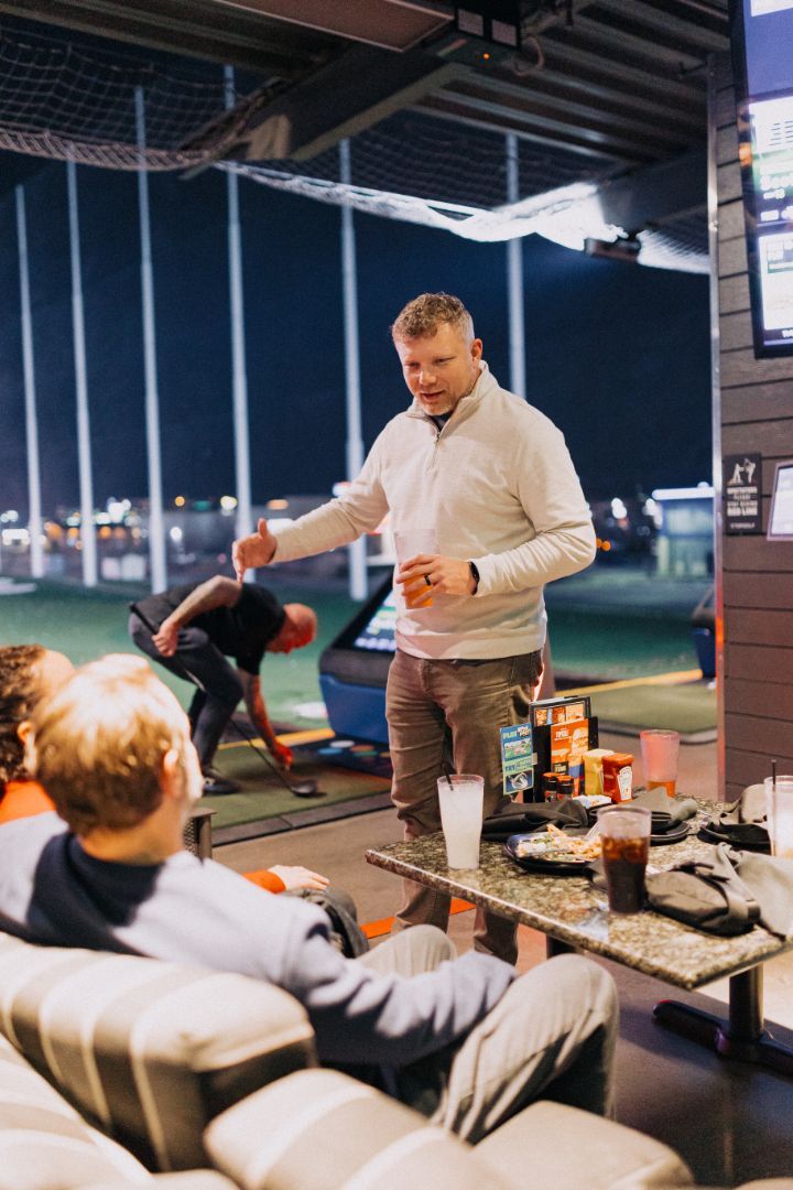A man is standing in front of a group of people sitting at a table.