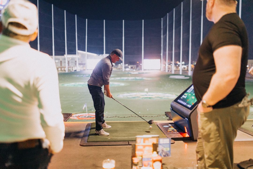 A man is swinging a golf club on a golf course at night.