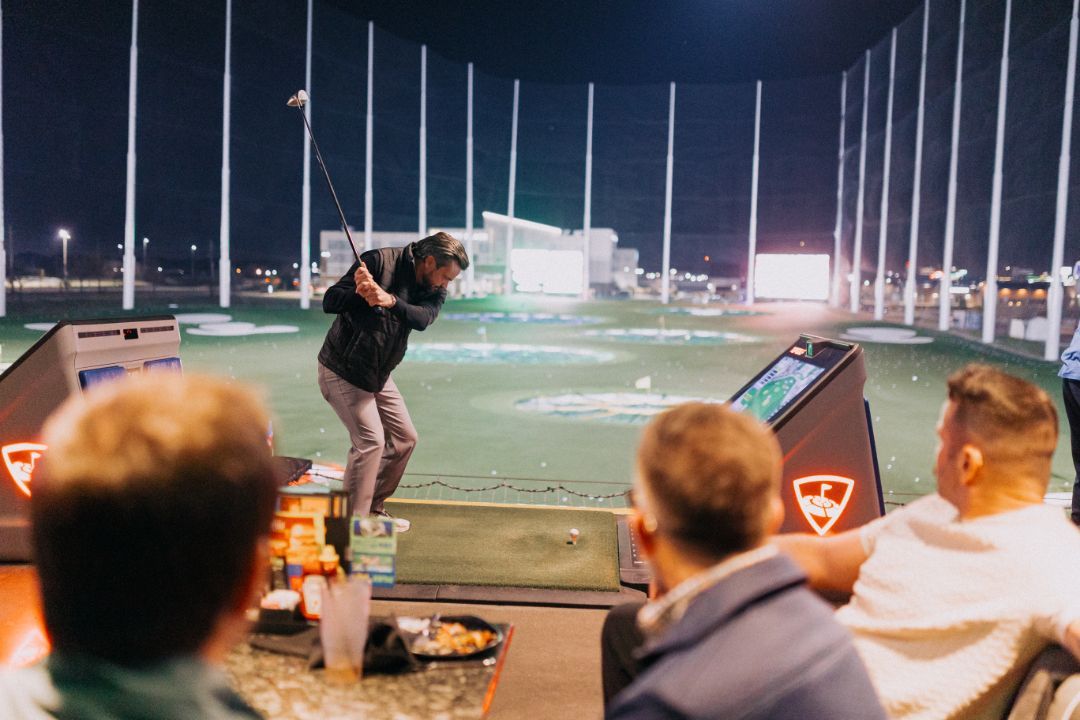 A group of men are watching a man swing a golf club on a golf course.