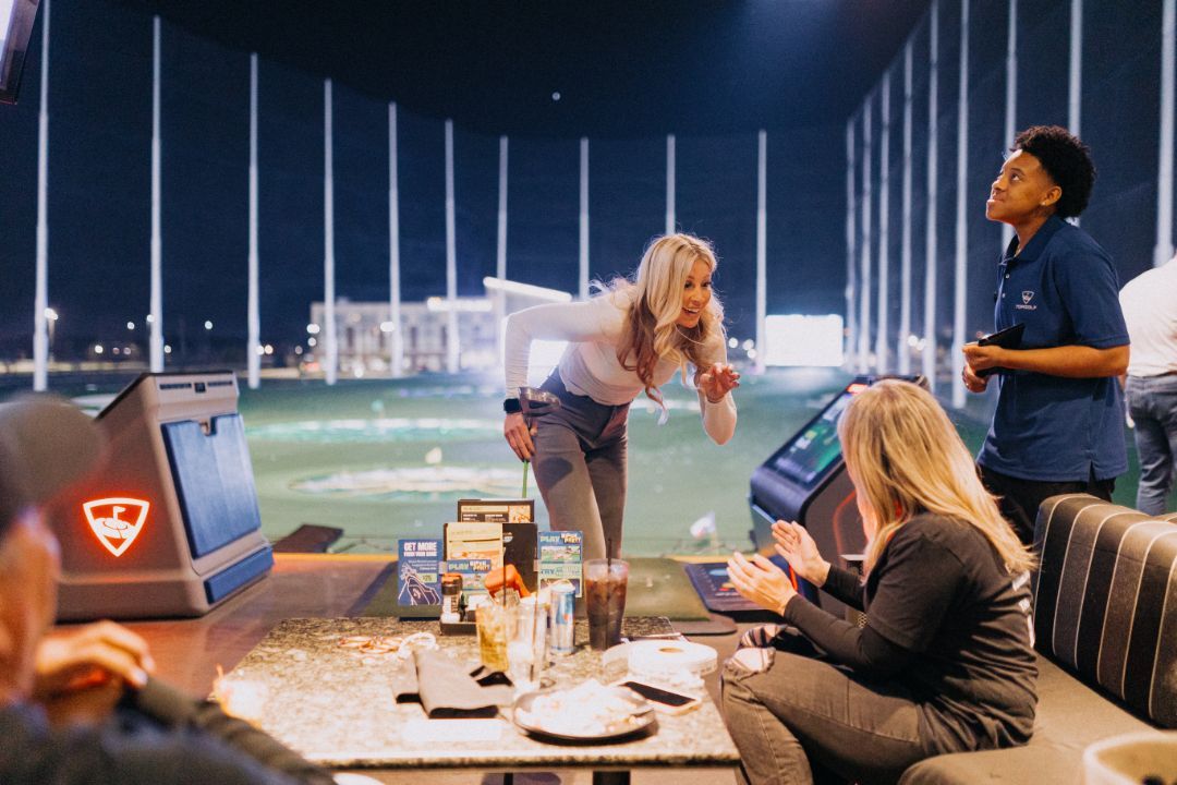 A group of people are sitting at a table in front of a golf course.