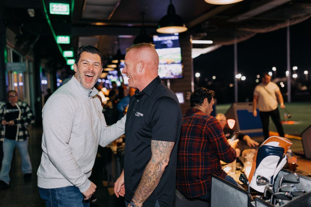 Two men are laughing and shaking hands in a bar.