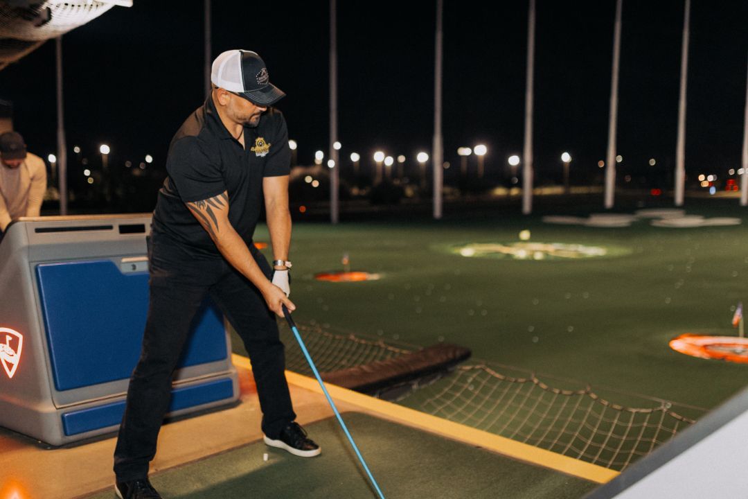 A man is swinging a golf club on a golf course at night.