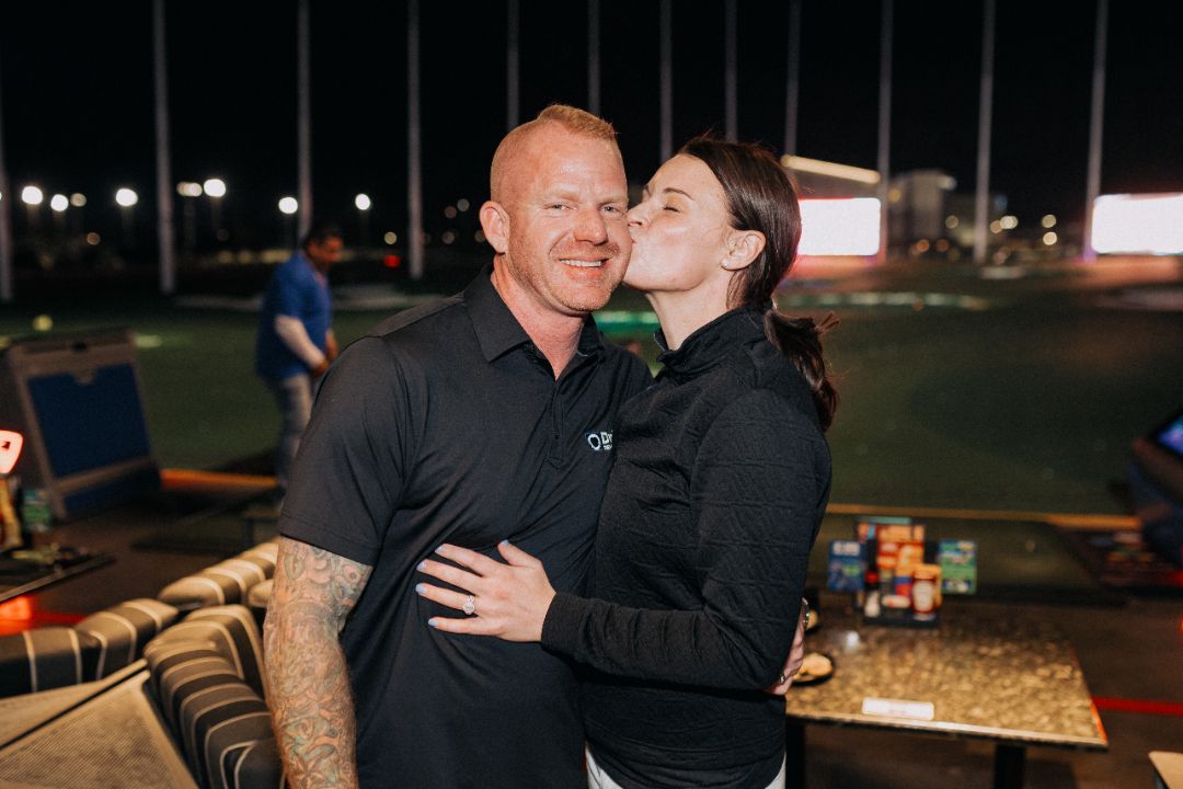 A man and a woman are standing next to each other and the woman is kissing the man on the cheek.