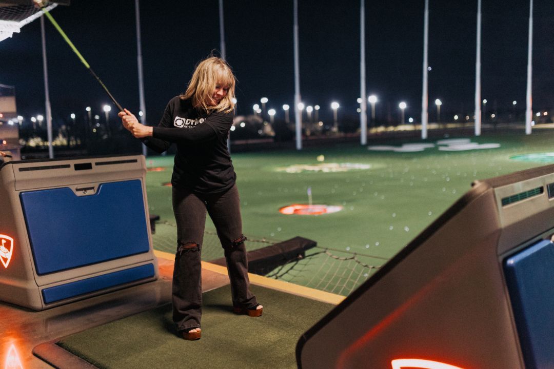 A woman is swinging a golf club on a golf course at night.